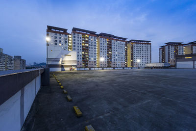 Road by illuminated buildings against sky at dusk