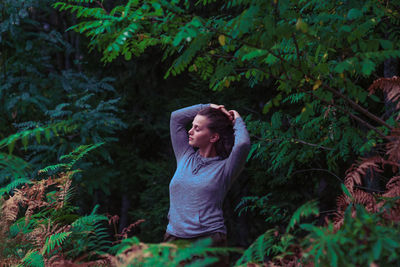 Beautiful young woman with hands in hair standing at forest