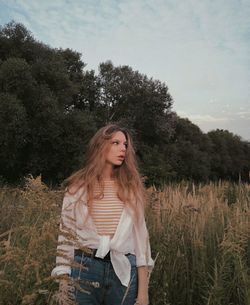 Young woman standing on field against sky