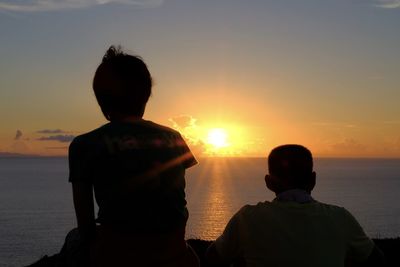 Rear view of silhouette man and woman standing at beach during sunset