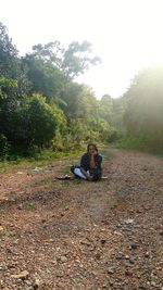 Young man sitting on land against sky