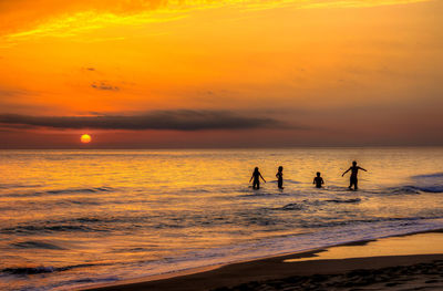 Silhouette people on beach against sky during sunset