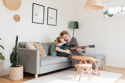 Daughter giving mother a hug whilst she plays guitar at home