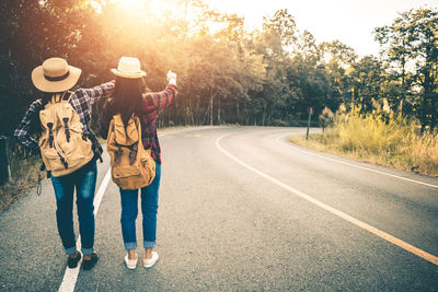 Rear view of friends standing on road against trees