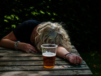 Woman drinking beer while holding pills on table