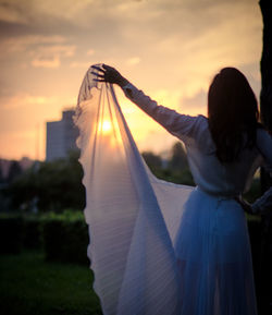 Rear view of woman standing on field against sky during sunset