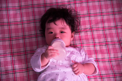 Close-up portrait of cute baby holding milk bottle while lying on blanket