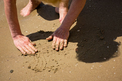 Elderly unrecognizable woman touching the wet sand on the seashore