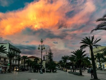 Street by palm trees against sky at sunset