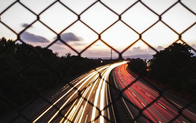 Light trails on chainlink fence against sky during sunset