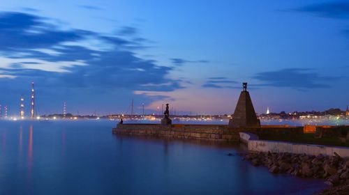 Illuminated building by sea against sky at dusk