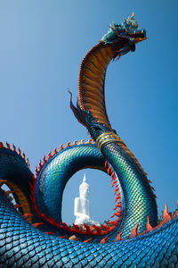 Low angle view of dragon and buddha statue against blue sky