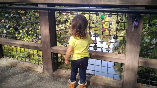 Rear view of girl standing against love locks hanging on railing