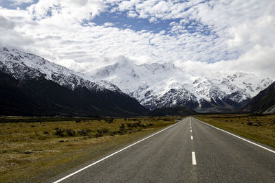 Road leading towards snowcapped mountains against sky