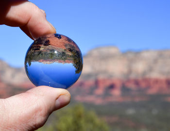 Cropped hand holding crystal ball against sky