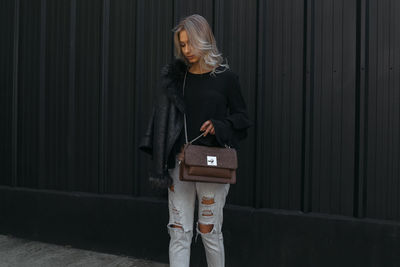 Young woman with purse standing on footpath by wall