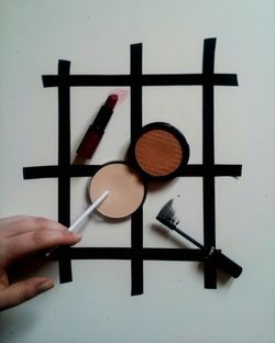 High angle view of powder compact and lipstick with cropped hand on table