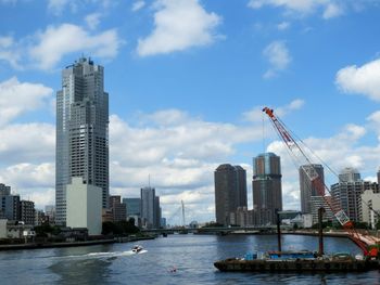 Crane over sumida river amidst buildings against sky