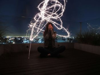 Woman sitting with illuminated lights against sky at night