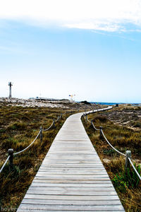 Boardwalk leading towards shore against sky