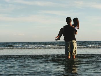 Rear view of father carrying daughter in sea against sky