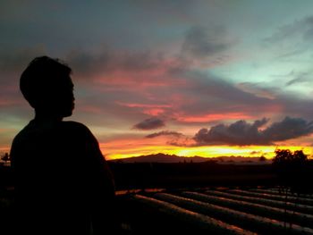 Rear view of silhouette man on field against sky during sunset