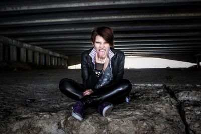 Full length of young woman showing rock sign under bridge