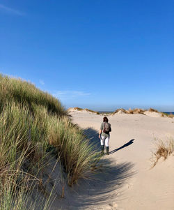 Man walking on beach against clear blue sky