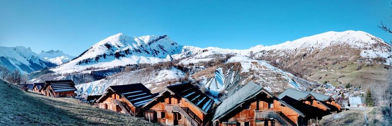 Panoramic shot of snow covered houses and mountains against blue sky