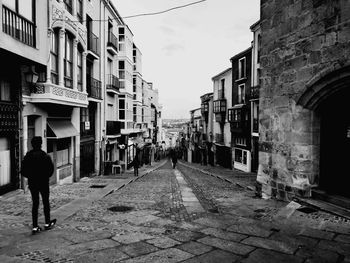 Rear view of woman walking on street amidst buildings in city