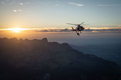 Military man getting down from helicopter against sky during sunset