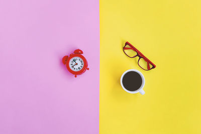 Directly above shot of coffee cup with pink petals against yellow background