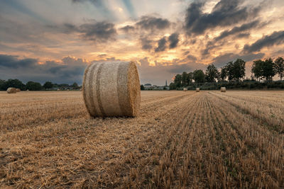 Hay bales on field against sky during sunset