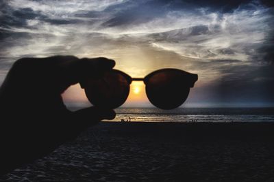 Silhouette hand on beach against sky during sunset