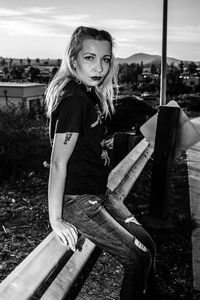 Young woman sitting on railing against sky