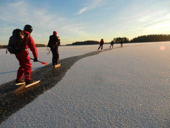 People ice skating on frozen lake against sky