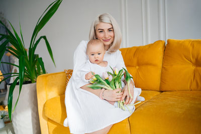 Mother with child in white clothes on a yellow sofa bouquet of flowers tulips spring