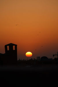 Silhouette birds flying against orange sky