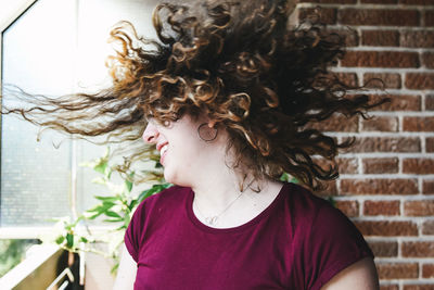 Happy young woman tossing hair against wall