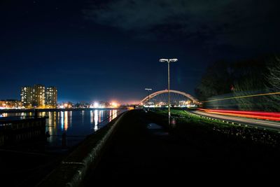 Light trails on road by river against sky at night