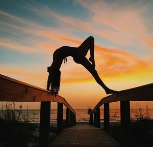 Silhouette woman on railings over footbridge at beach against sky during sunset