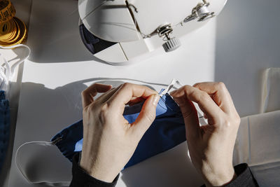 Top view of crop tailor sewing rubber band to fabric mask in workshop