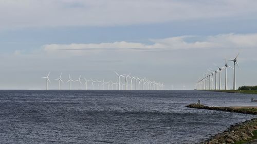 Scenic view of group of wind turbines in sea against sky