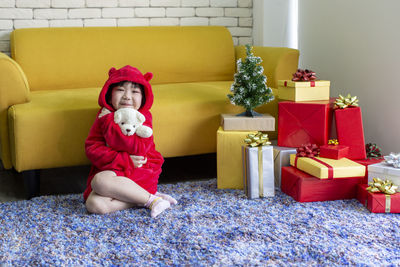 Full length portrait of cute girl holding teddy bear while sitting by gift boxes at home