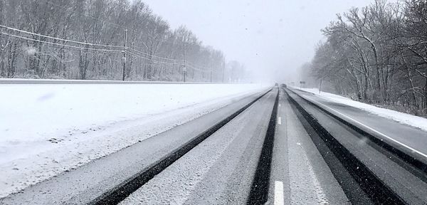 Snow covered road amidst trees during winter