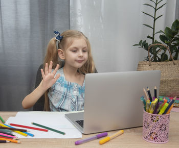 Girl gesturing while video conferencing over laptop on table