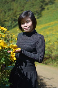 Portrait of smiling woman standing on yellow flowering plants