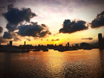 Silhouette city by sea against sky during sunset