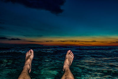 Low section of man above sea at sunset