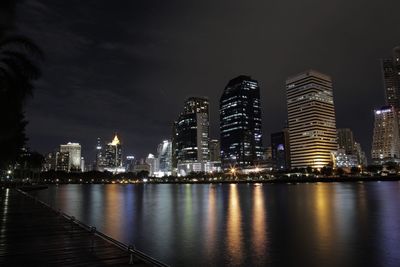 Illuminated buildings by river against sky at night